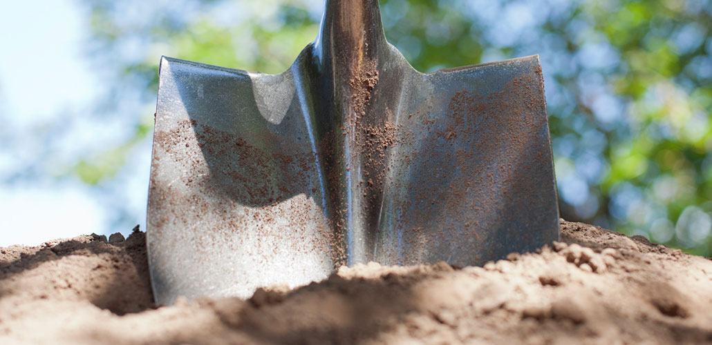 Image of a shovel standing upright in a dirt patch with trees in the background, depicting rebuilding efforts after wildfires by Rebuilding Together